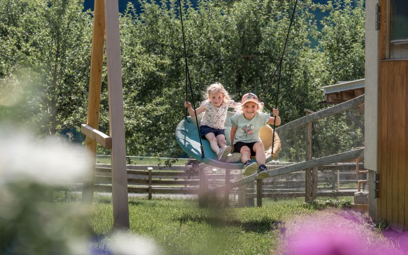 Zwei Kinder schaukeln auf der Nestschaukel am Spielplatz des Tobhartbauers
