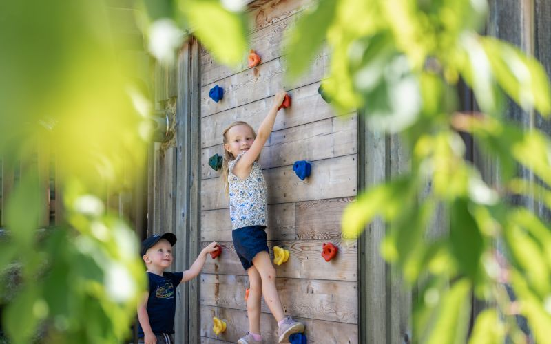 Zwei Kinder klettern an der Holzkletterwand auf dem Spielplatz des Tobhartbauers