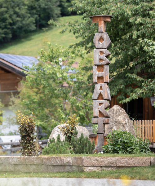 Holzskulptur mit dem Schriftzug Tobhart im Garten des Bauernhofs