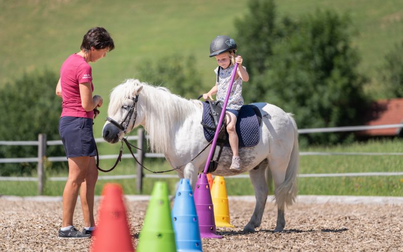 Reitpädagogin Ilona Hutter begleitet ein Kind auf einem weißen Pony am Tobhartbauer